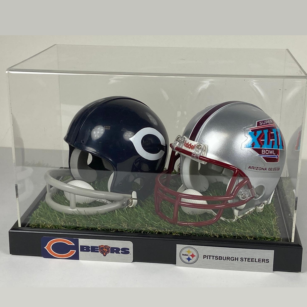 Two football helmets from the Chicago Bears and Pittsburgh Steelers in a display case with grass base.