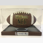 Wilson NFL football in a clear display case with a wooden base, signed by Tom Brady.
