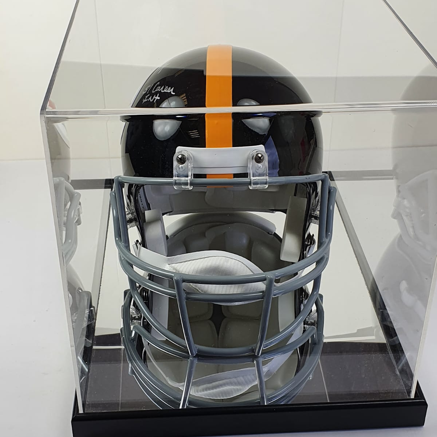 Black football helmet with orange stripe in a clear display case.