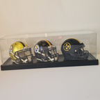 Three football helmets in a clear display case on a white surface.