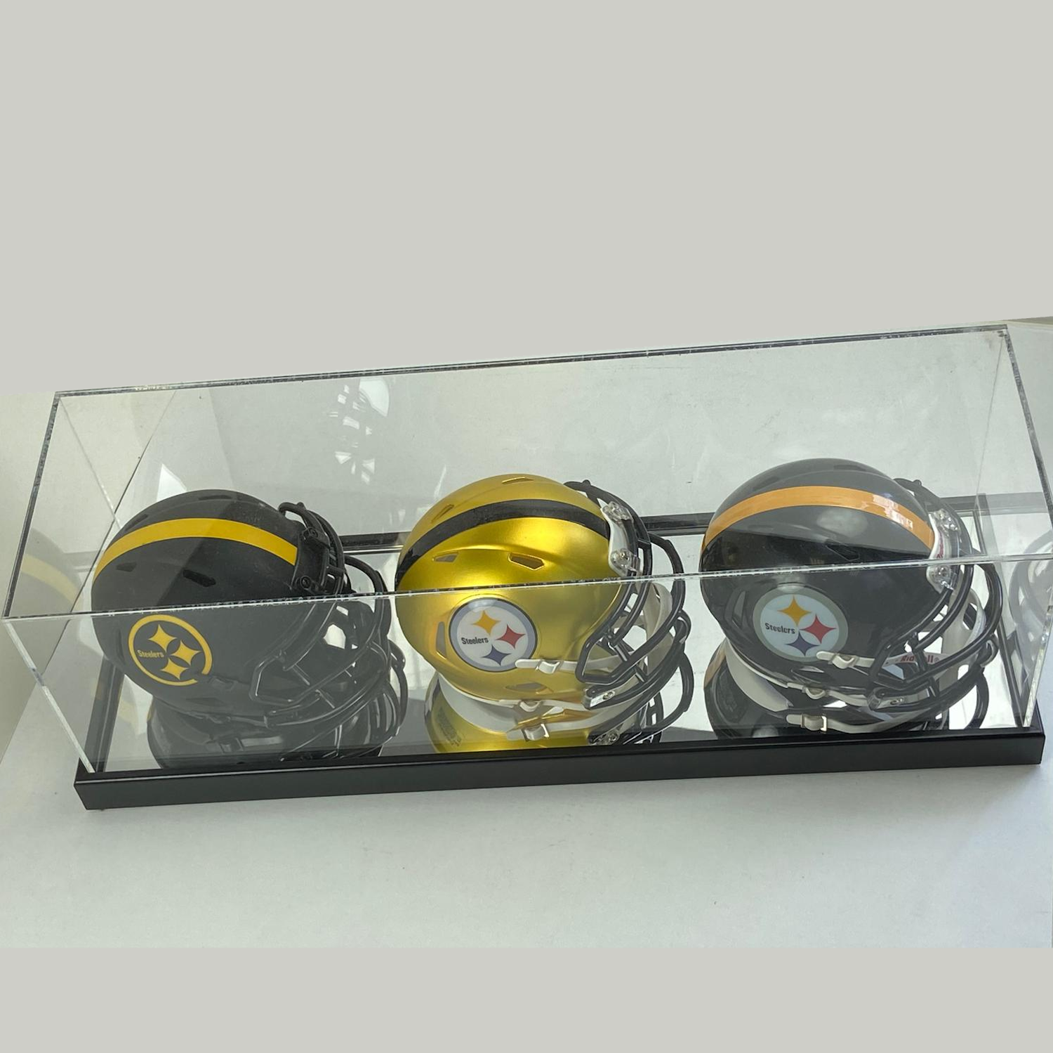 Three football helmets with logos in a clear display case on a white background