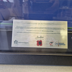 Certificate of Authenticity for a ceramic poppy with branding and logos on a reflective surface.