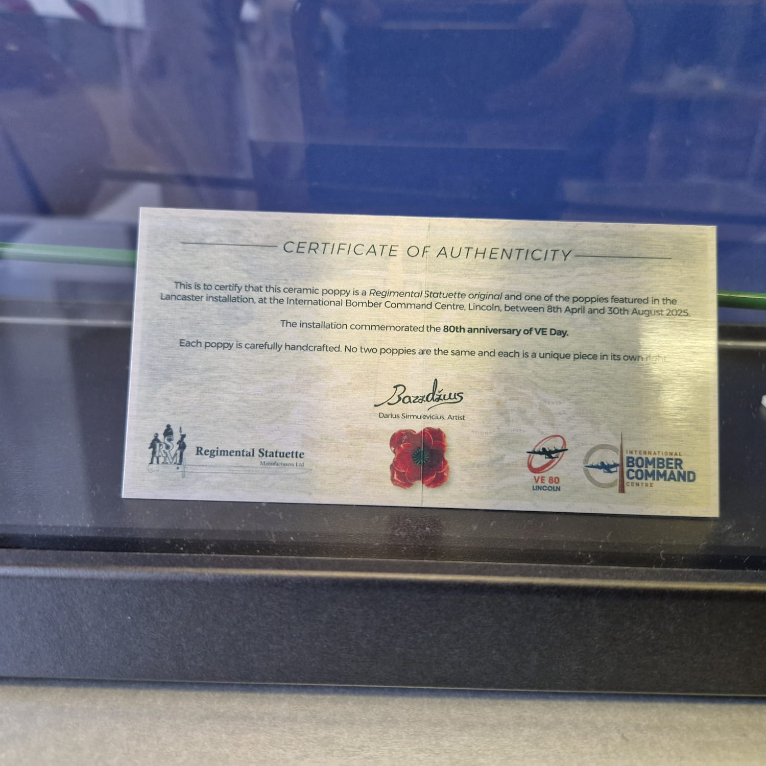 Certificate of Authenticity for a ceramic poppy with branding and logos on a reflective surface.